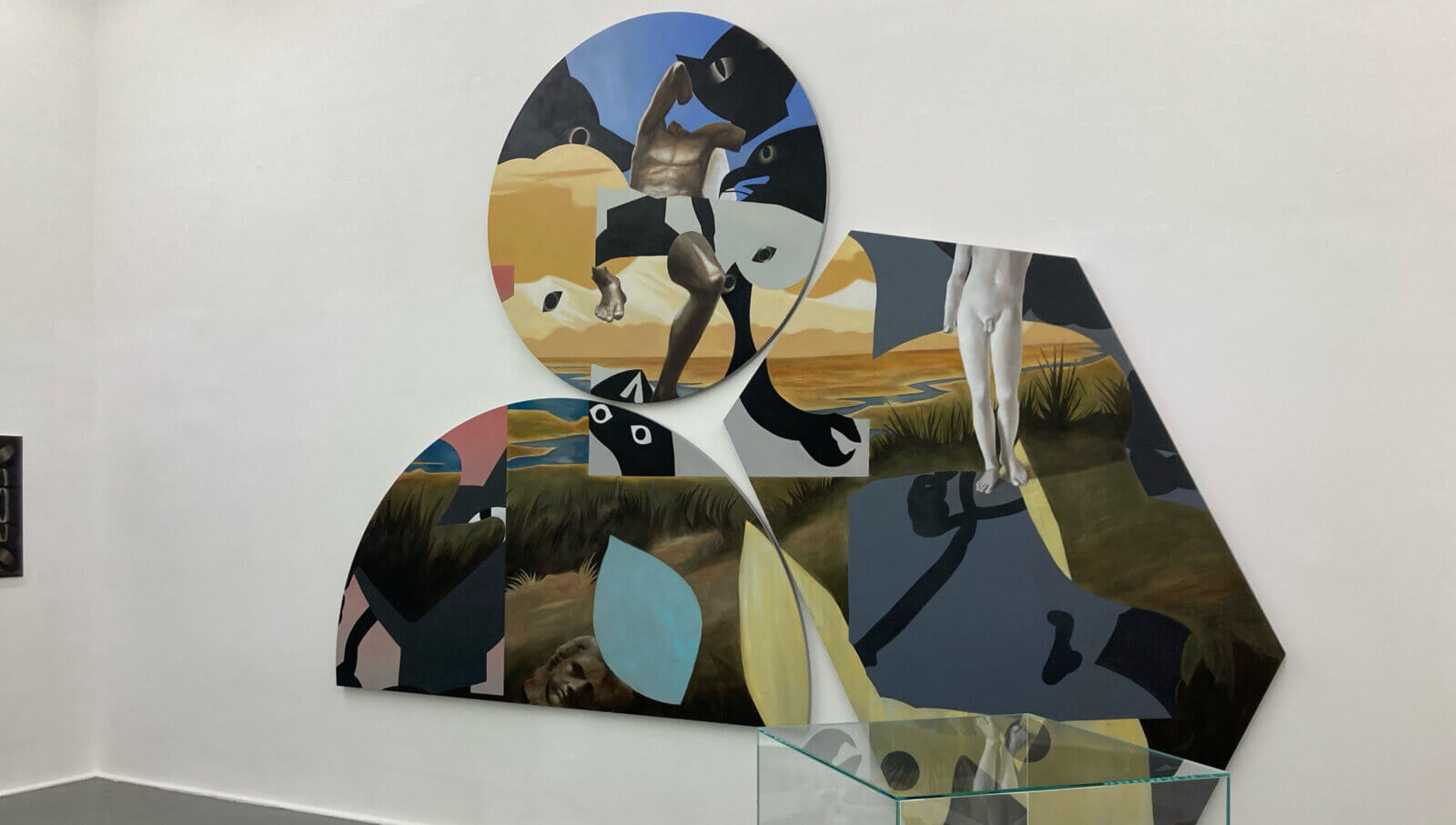 Dreigeteiltes abstraktes Bild aus abstrakten Formen an der Wand, davor ein kleine abstrakte Skulptur in einer Standvitrine