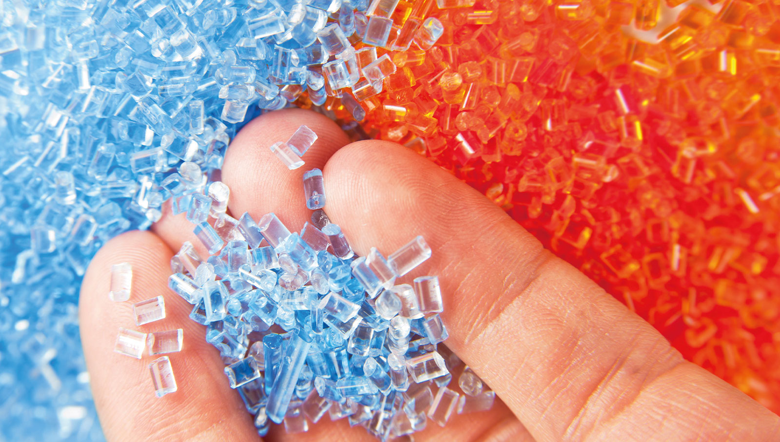 Close-Up Finger heben blaues und orangenes Kunststoffgranulat
