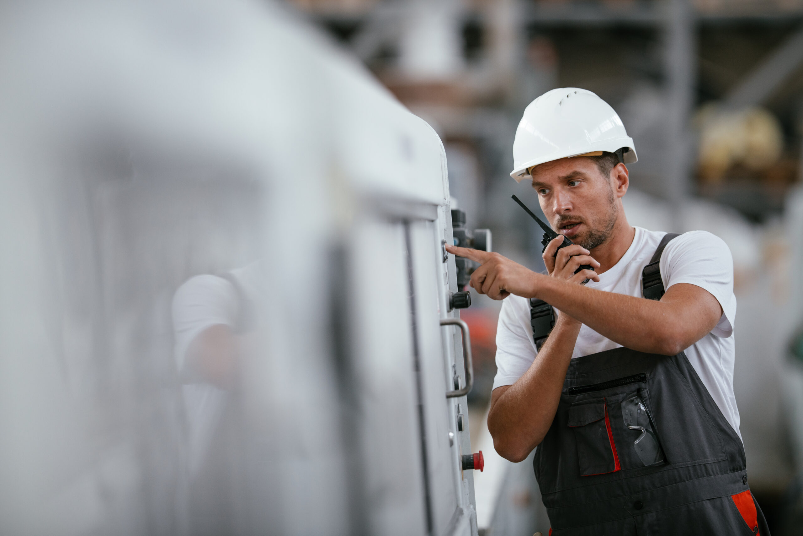 Junger Ingenieur mit Helm auf und Funkgerät in der Hand macht Produktionskontrolle