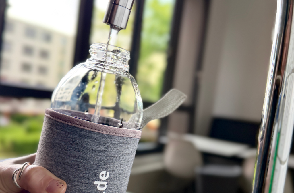eine Flasche mit BEST GRUPPE Logo wird unter dem Hahn mit Wasser befüllt