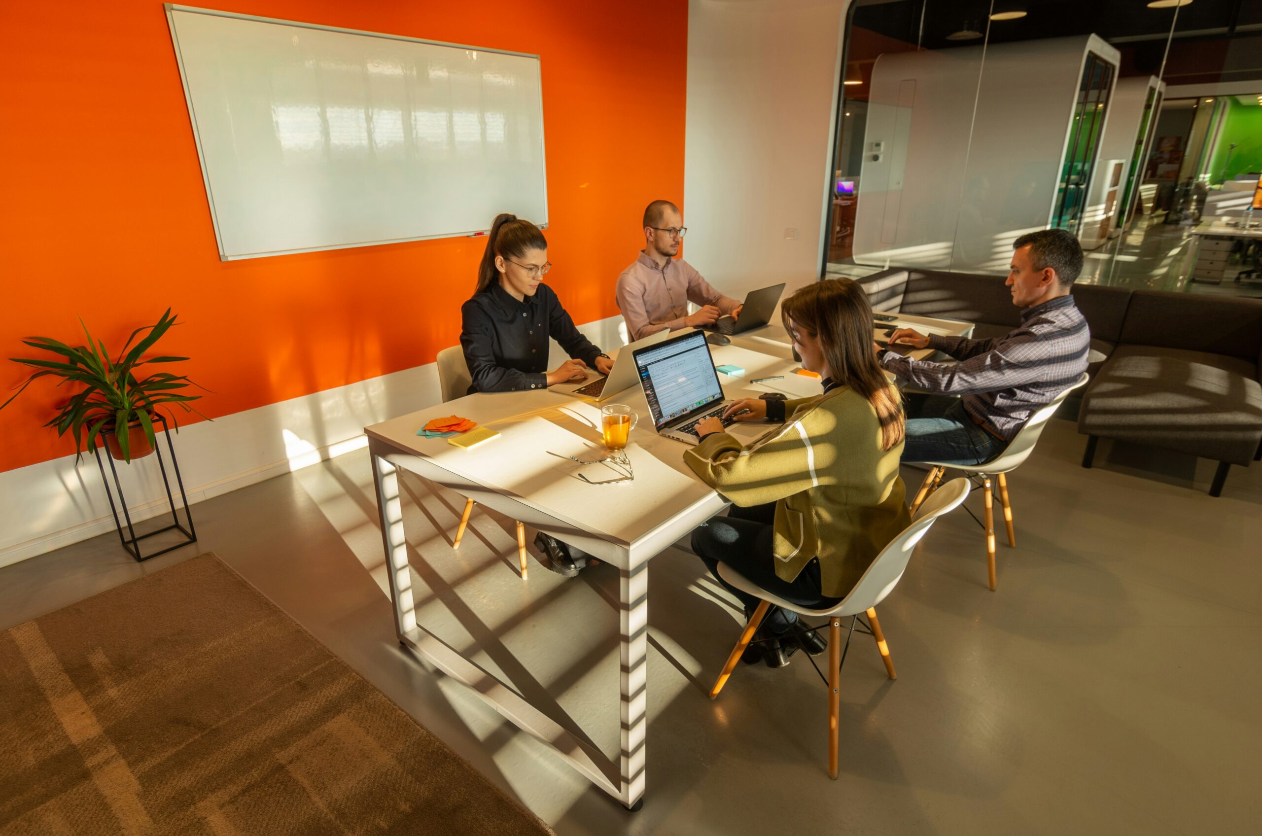 4 Menschen sitzen am Tisch und arbeiten mit Laptop
